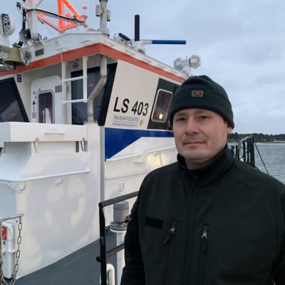 En sjöbevakare i mörka kläder står framför en båt. 