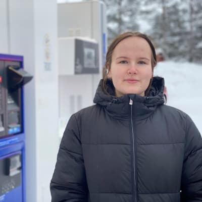 Roosa-Maria Mattila seisoo huoltoasemalla polttoainepumppujen vieressä.