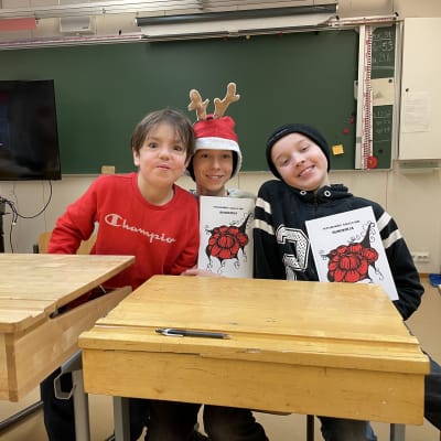 Kolme koululaista hymyilee ja hassuttelee käsissään runokirja, jonka heidän koulunsa on tehnyt.