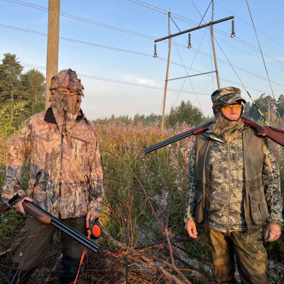 Kaksi maastopukuihin pukeutunutta metsäsätäjää aamuauringossa, molemmilla halukot. Taustalla sähköjohtoa ja hormaa.