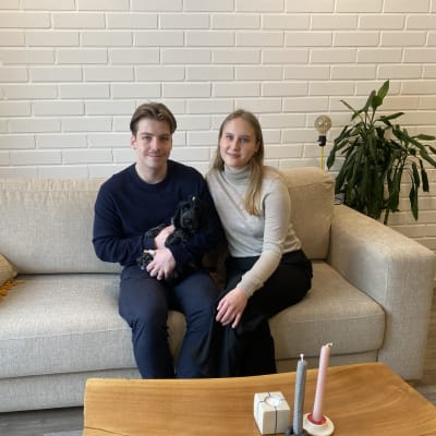 Ett ungt par som sitter i en soffa med en hundvalp i famnen.