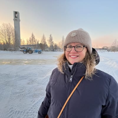 Anna Valtari seisoo Lakeudenpuiston jäädytettävällä luistinradalla. Taustalla traktori vesisäiliöineen ja Lakeuden ristin torni.