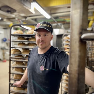 MBakeryn yrittäjä Mikko Hietala seisoo leipäkärryn edessä ja katsoo kohti kameraa. 