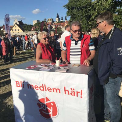 Två personer i röda västar vi ett bord med texten "Bli medlem här!"