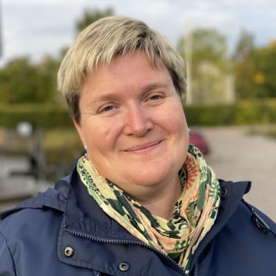 Ung kvinna i blå kläder står och ler mot kameran.