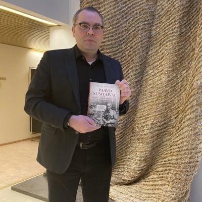 Jussi Niinistö seisoo kirja kädessään.