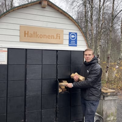 Valto Vaaraniemi seisoo polttopuuautomaatin edessä ja ottaa halkoja automaatista.