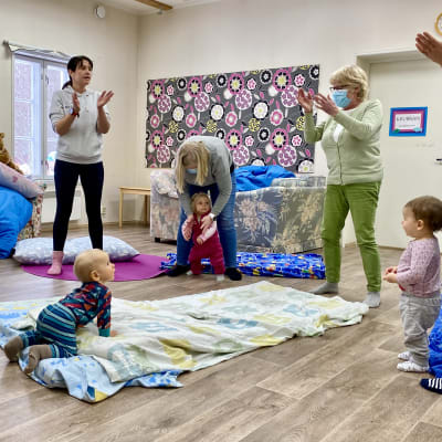 En mamma-barngrupp klappar i händerna och sjunger. En bebis tittar på de vuxna.