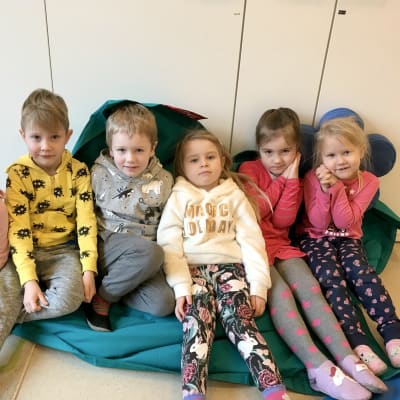 Sex dagisbarn sitter på en stor blå kudde.