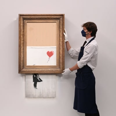 En man håller i tavlan Love is in the bin, dvs en målning med en flicka och en ballong som är halft sönderstrimlad i sin ram.