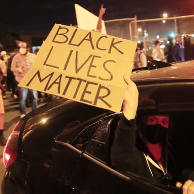 Bild på arm som håller ut skylt där det står att svarta liv är värda lika mycket ur en bil. 