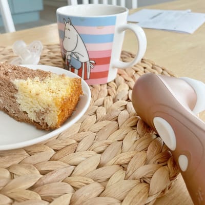 En vibrator ligger på köksbordet intill en kaffekopp, en napp och en tallrik med en tårtbit. 