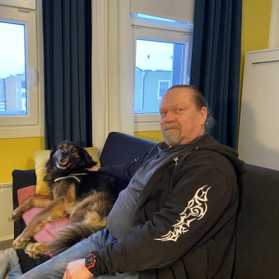 Luopioisten miniomakotitaloalueella asuva Petrus Kinnunen ja koiransa Massa istuvat sohvalla.  Asunnossa on vain 27 neliötä. 