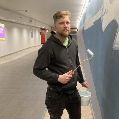 Taiteilija Topi Ruotsalainen maalaamassa seinään taideteosta.