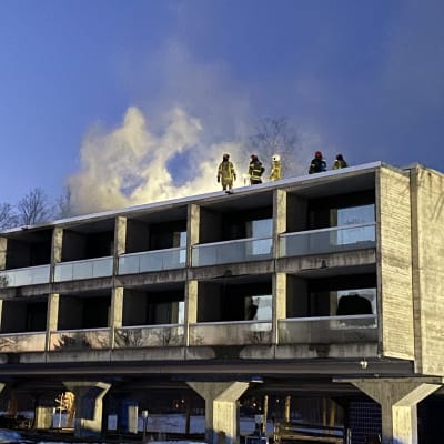 Pelastajia rakennuksen katolla, taustalla kohoaa savua. 