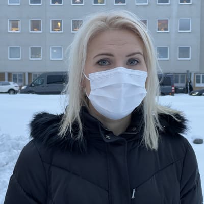 Kvinna i munskydd utomhus framför sjukhus.