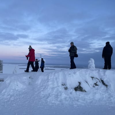Ihmiset vierailevat Kolin huipulla talvi-illan sinisessä pakkasessa. 
