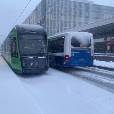 Ratikka ja bussi rinnakkain Tampereen lumisessa säässä.