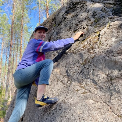 Boulderoinnin harrastaja kiipeilee isolla kivenlohkareella. 