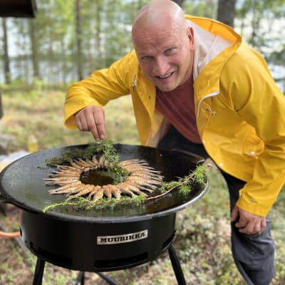 Keittiömestari Sauli Kemppainen maustaa katajan oksalla paistettuja muikkuja ulkopannulla.