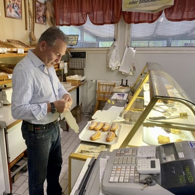 En man står bakom kassan på en bageributik och packar munkar i lådor.