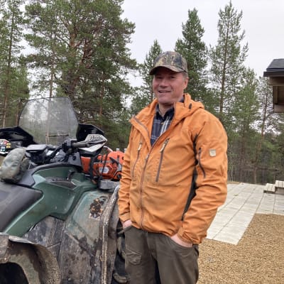 Osmo Seurujärvi seisoo mönkijän vieressä ja katsoo kameraan ja hymyilee.
