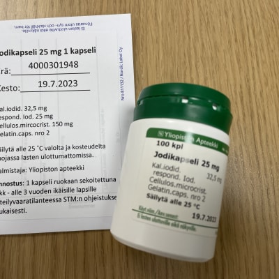 Kuvassa pienille lapsille tarkoitetun lääkejodin valkovihreä muovinen lääkepurkki ja sen vieressä paperilla käyttöohjeet.
