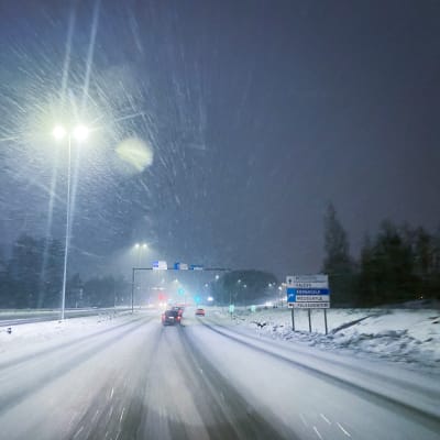 Bilar på en motorväg när det snöar och är mörkt. 