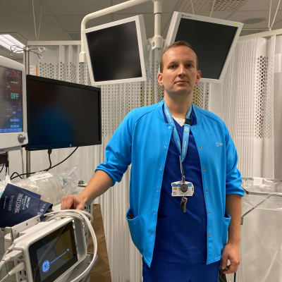 Ylilääkäri Mikko Franssila katsoo kameraan. Hänen ympärillään on erilaisia sairaalaympäristöön kuuluvia näyttöjä.