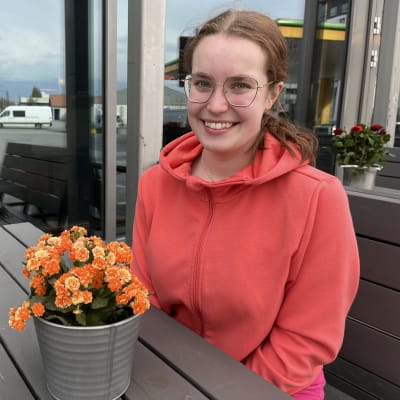 Hymyilevä Helmiina Sairberg istuu ulkona pöydän ääressä ja katselee eteenpäin. Pöydillä on kukkia.