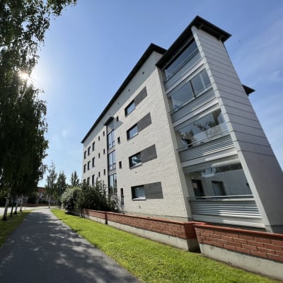 Kerrostalo jonka vieressä menee tie ja bussi. 