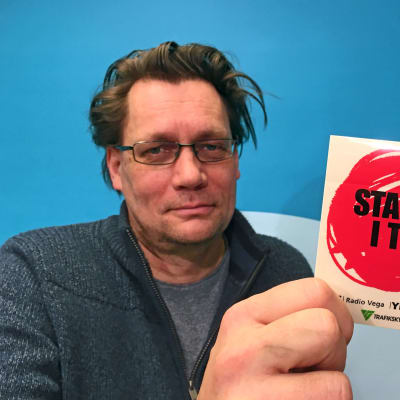 Mikael Kokkola visar upp ett klistermärke från kampanjen Stanna i tid.