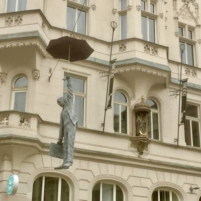En staty i Prag av en man med paraply som hänger i luften över gatuhöjd.