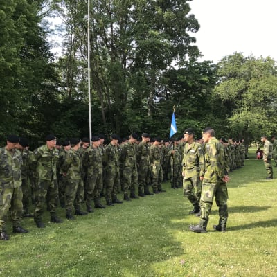 Två militära befäl granska grönklädda soldater uppställda på en gräsmatta.