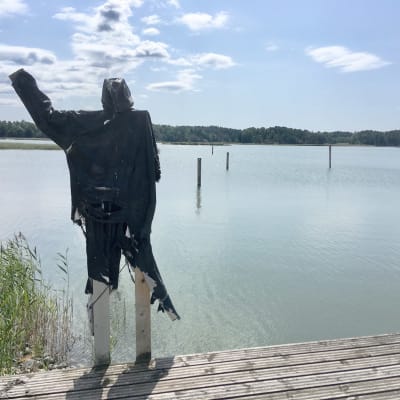 en svart figur gjord av tyg och trä vinkar ut mot havet.
