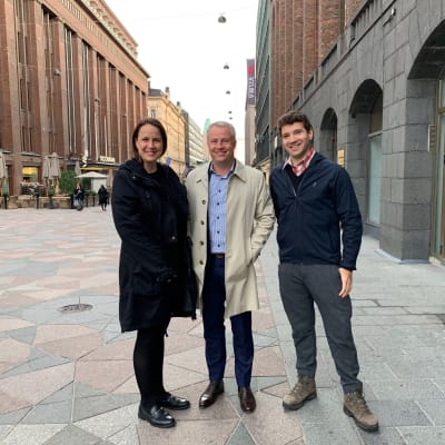 Från vänster står Veronika, Marcus och Ted mellan Akademiska Bokhandeln och Stockmanns varuhus i Helsingfors, leende mot kameran och med ytterkläder på.