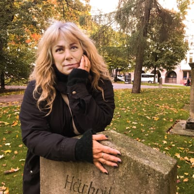 Stina Wollter lutar mot en gravsten i en höstig park i Helsingfors.