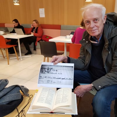 En man sitter och håller upp ett papper.