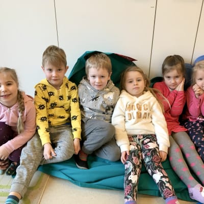 Sex dagisbarn sitter på en stor blå kudde.