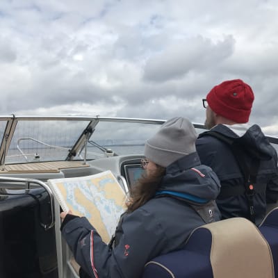 Nainen lukee karttaa veneessä, jota mies ohjaa Vesijärvellä.