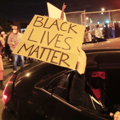 Bild på arm som håller ut skylt där det står att svarta liv är värda lika mycket ur en bil. 