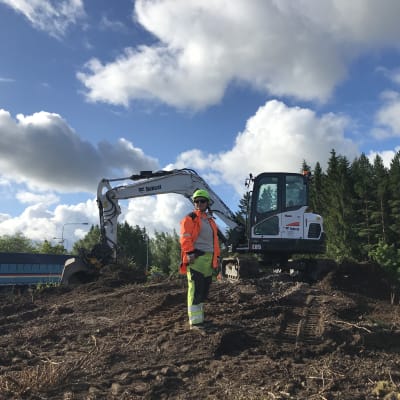 Kvinna i reflexkläder står bredvid en grävmaskin i en rondell som håller på att byggas om.