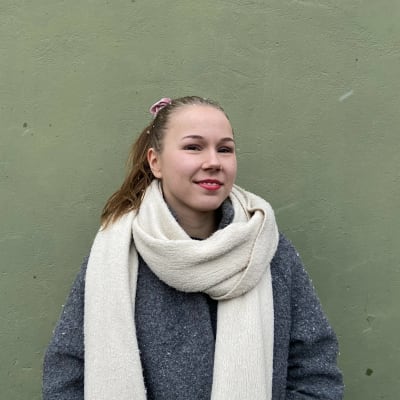 Sara står och ler framför en grön stenvägg.