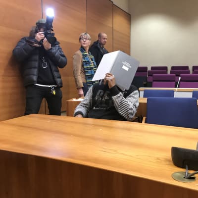 En person täcker sitt ansikte i en rättegångssal. 