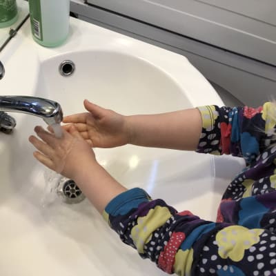 Lapsi pesee käsiä vesihanan alla.