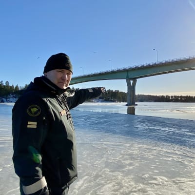 En sjöbevakare står och pekar ut mot isen under Emsalö bro.