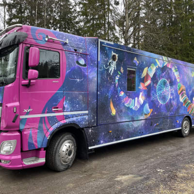Kirjastoauto Kosmos avaruudessa mutkitteleva kirjapino kyljessään on pysäköitynä Tampereen Tasanteen kirjastoauton pysäköintipaikalle.
