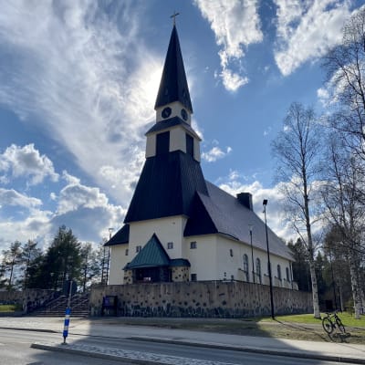 Rovaniemen kirkko kesäpäivänä, aurinko paistaa kirkontornin takaa