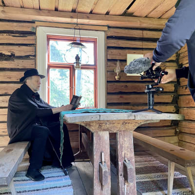 Lasse Lyytikäinen lukee kirjaa pöydän ääressä sekä  kameran edessä.