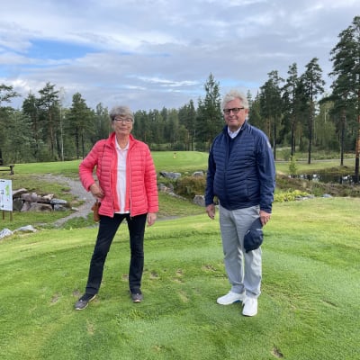 Porträtt av Annika Colérus och Henrik Sarajas som står bredvid varandra och ser in i kameran. De står på en golfbana, i bakgrudnen finns terränghinder. 